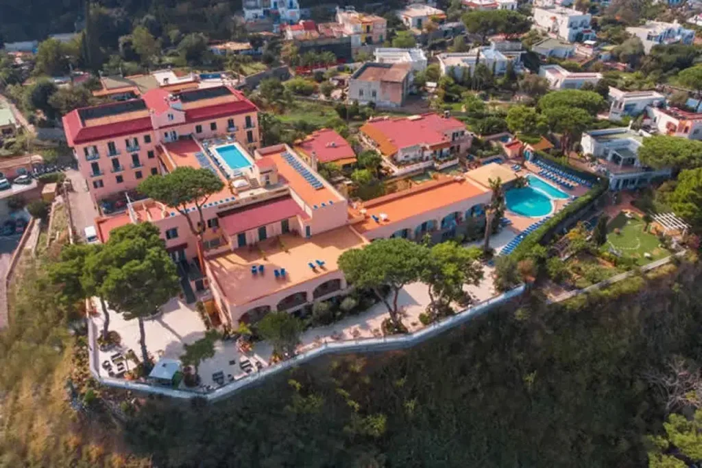 Veduta aerea del complesso alberghiero con piscine, giardini e tetti rossi sulla costa