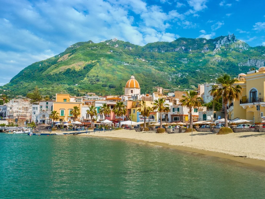 Vista panoramica del borgo colorato di Ischia con spiaggia e montagne verdi