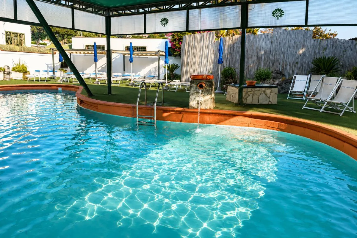 Piscina termale coperta con acqua azzurra, fontana e lettini nel giardino